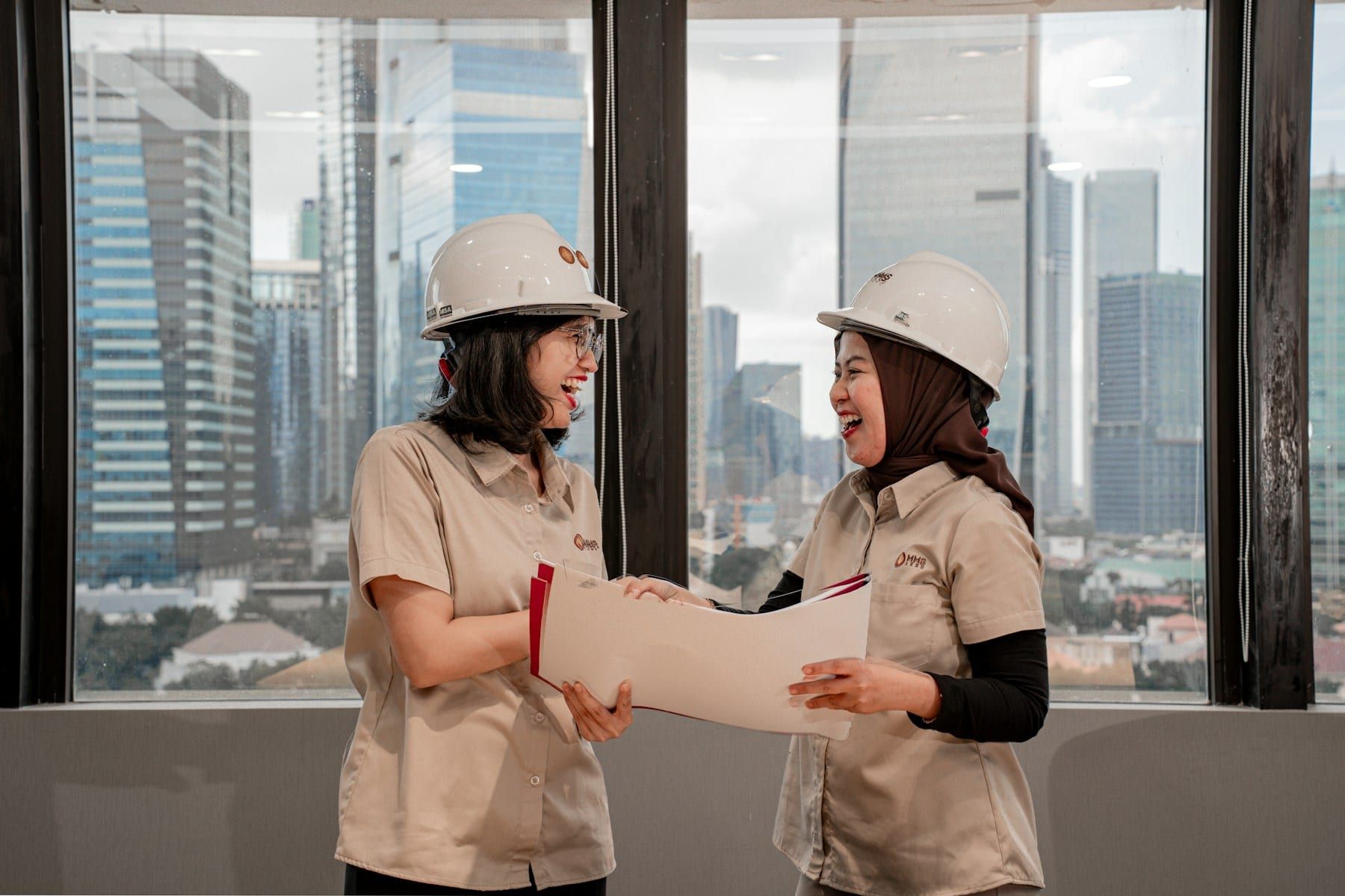 Two engineers in hard hats reviewing a document in a city office